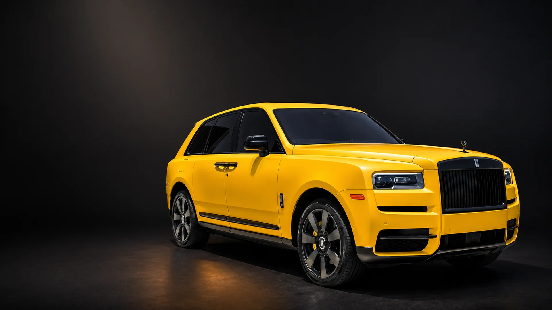 Yellow Rolls-Royce Cullinan with blacked-out wheels and dark window tint, against a dark studio backdrop
